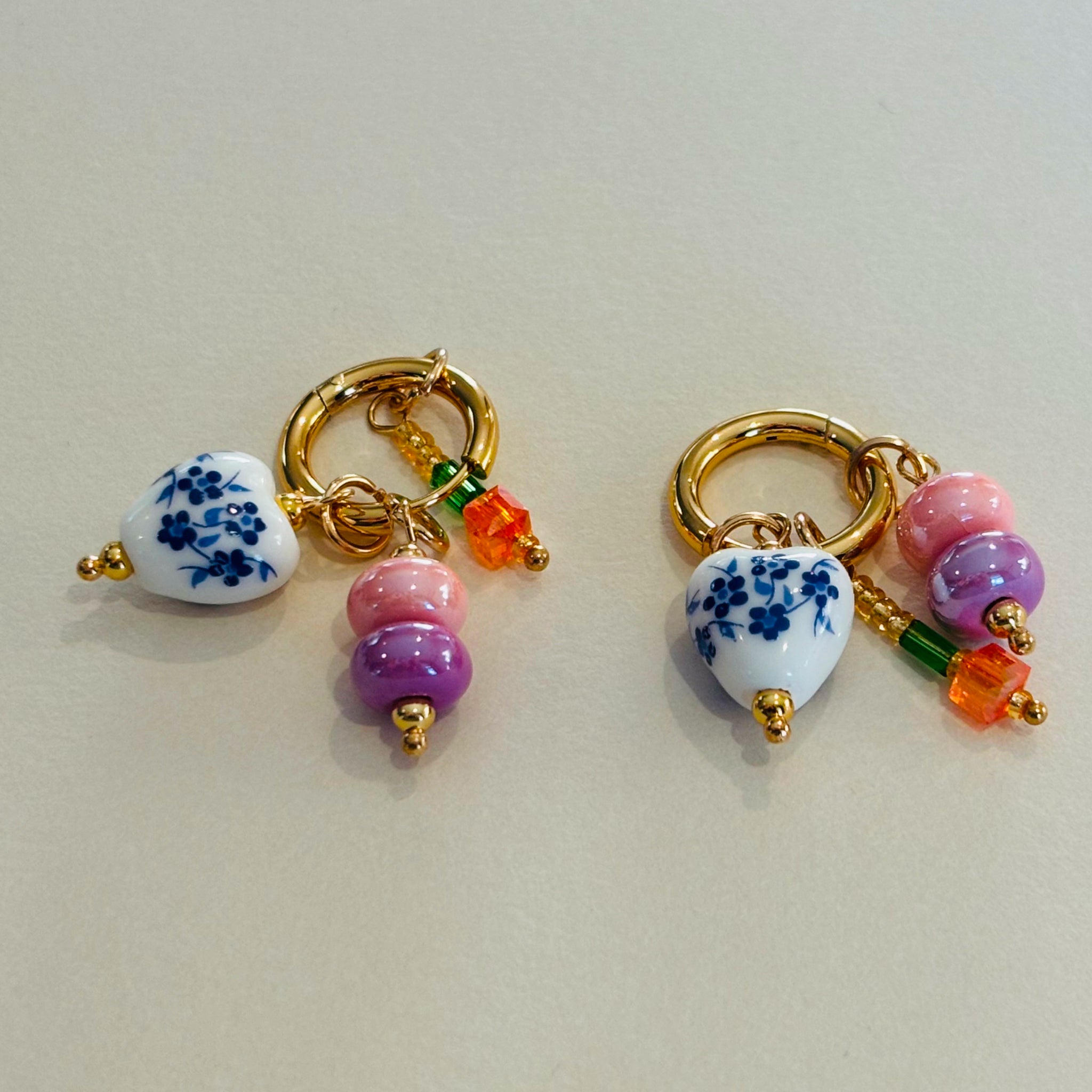 Pair of gold hoop earrings with heart-shaped ceramic beads and colorful glass beads.