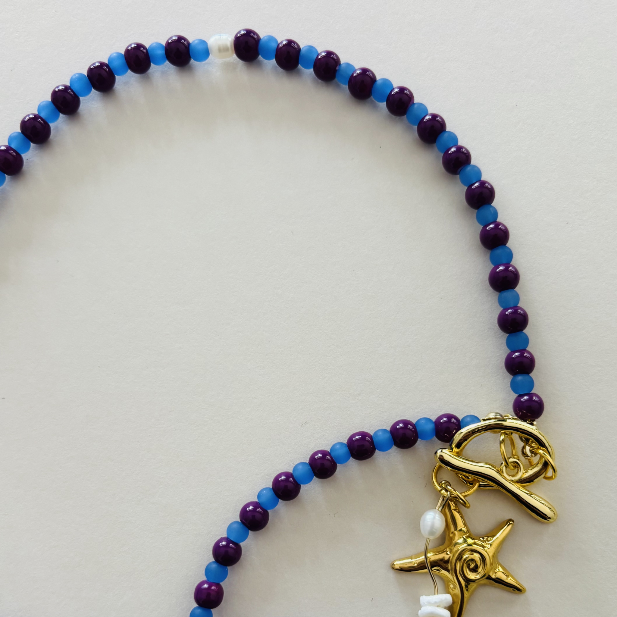 Beaded bracelet with blue and purple beads and a gold starfish charm